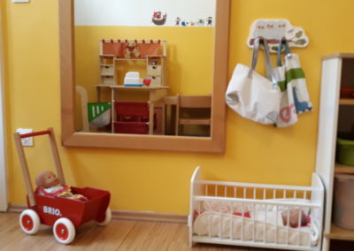 Raum der Kindergruppe: Puppen-Gitterbett, Puppen-Kinderwaagen und Spiegel