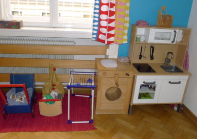 Children's group room: play kitchen with washing machine, laundry rack, doll scales and doll crib.