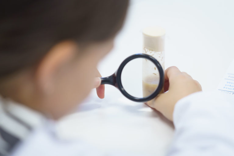 Child in lab coat examines liquid with magnifying glass