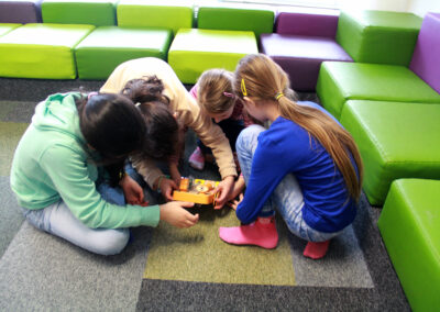 Vier Mädchen sitzen am Boden und beugen sich über einen Roboter.