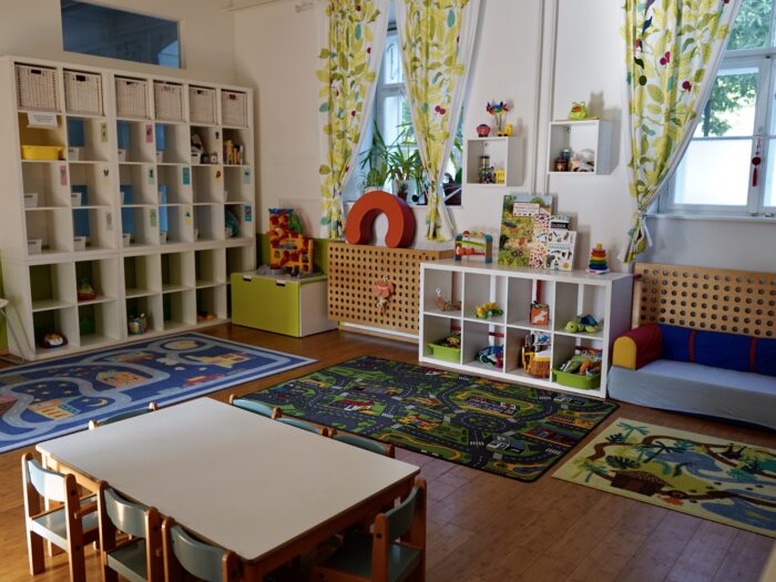 Raum der Kindergruppe mit Regalen, Spielteppichen, Couch und Sitzgruppe für Kinder