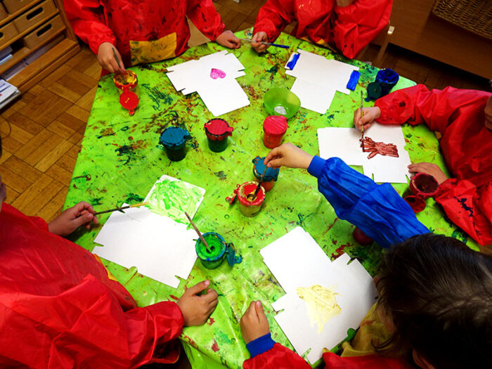 Kinder in roten Umhängen malen Bilder mit Wasserfarben