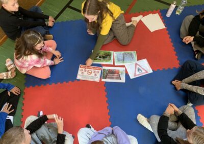 Children and an adult sit on a mat on the ground and look together at signs about the risk of forest fires.